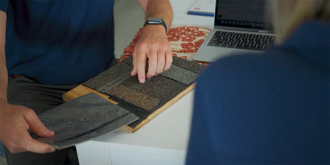 Person selecting textured material samples on a table, with a laptop in the background.