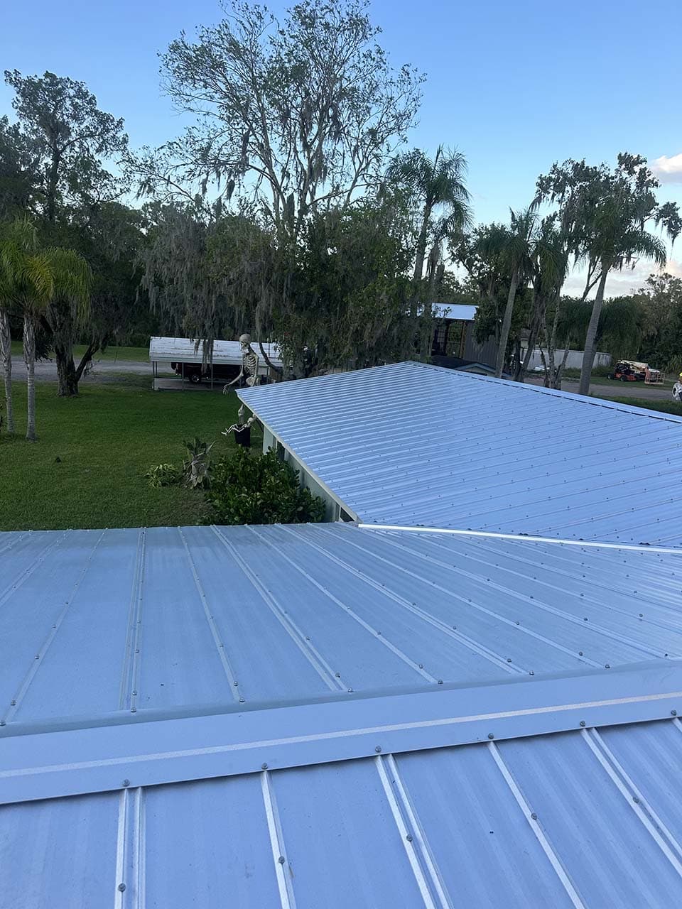 Metal roofs on residential buildings surrounded by trees and grass under a clear blue sky.