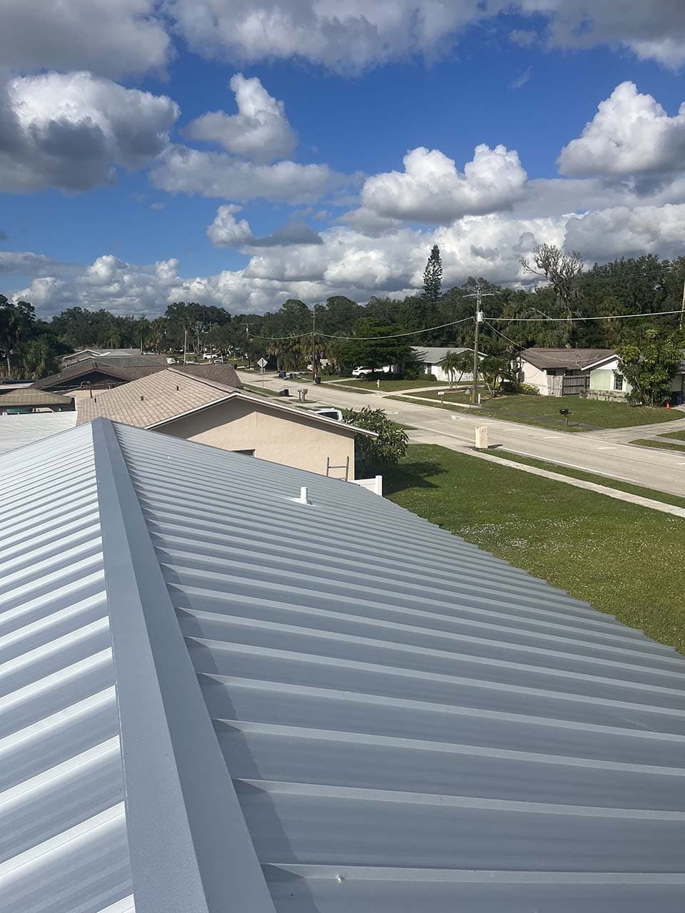 Metal roof view overlooking suburban neighborhood with cloudy blue sky.