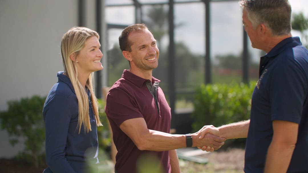 Two smiling individuals shaking hands with a man outdoors, showcasing a friendly meeting.