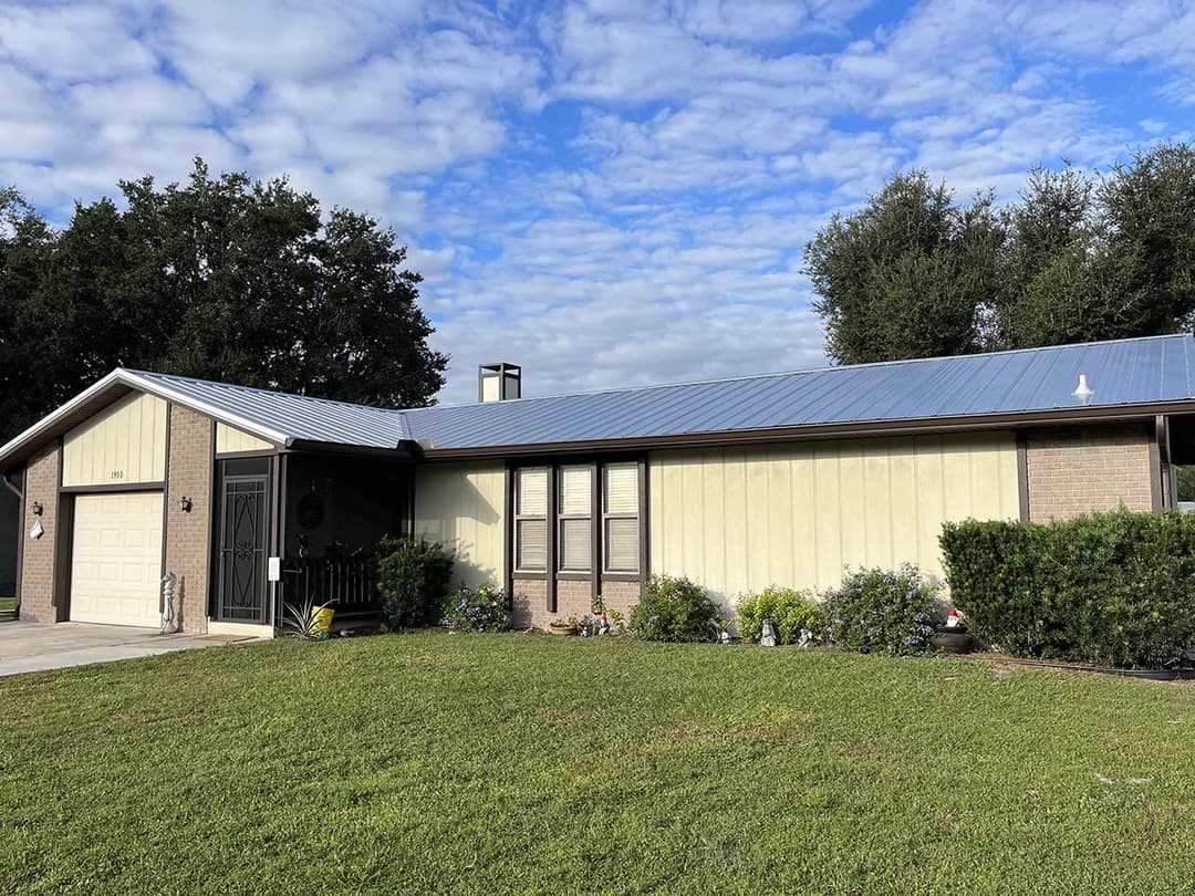 Single-story house with a metal roof, well-maintained lawn, and decorative shrubs.